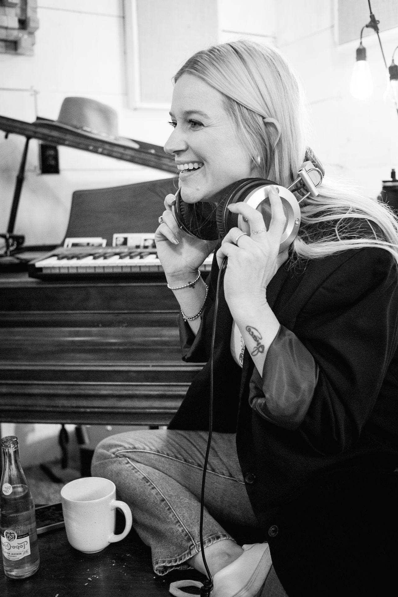 Person sitting by a piano, holding headphones, with a soda bottle and mug on the table.