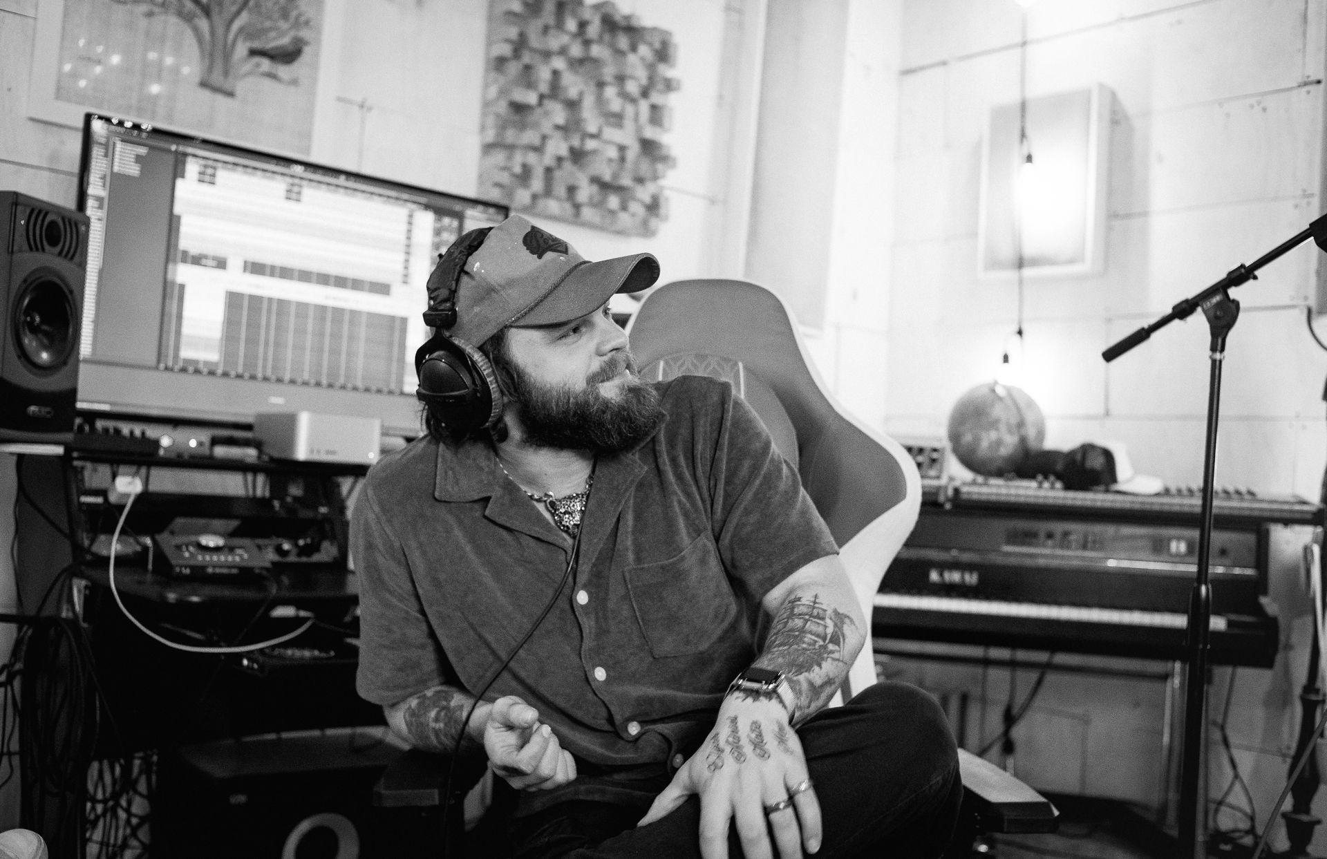 Person with headphones sitting in a studio, working on music with a computer and audio equipment.