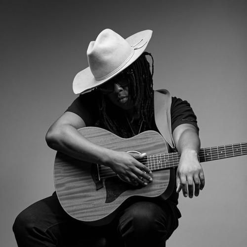 Black and white photo of a person in a hat playing an acoustic guitar.