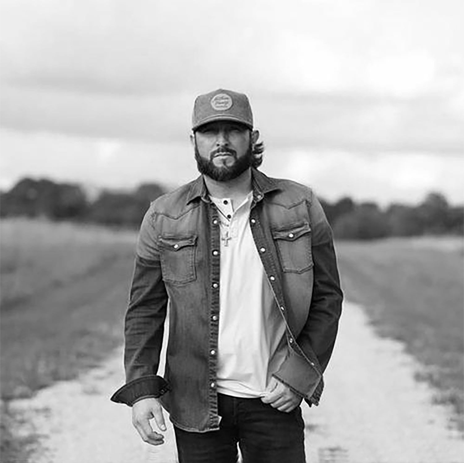 Man in denim shirt and cap walking on a rural path.